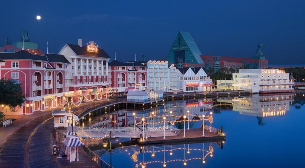 Fachada iluminada do Disney’s BoardWalk Inn à noite, refletida no lago.