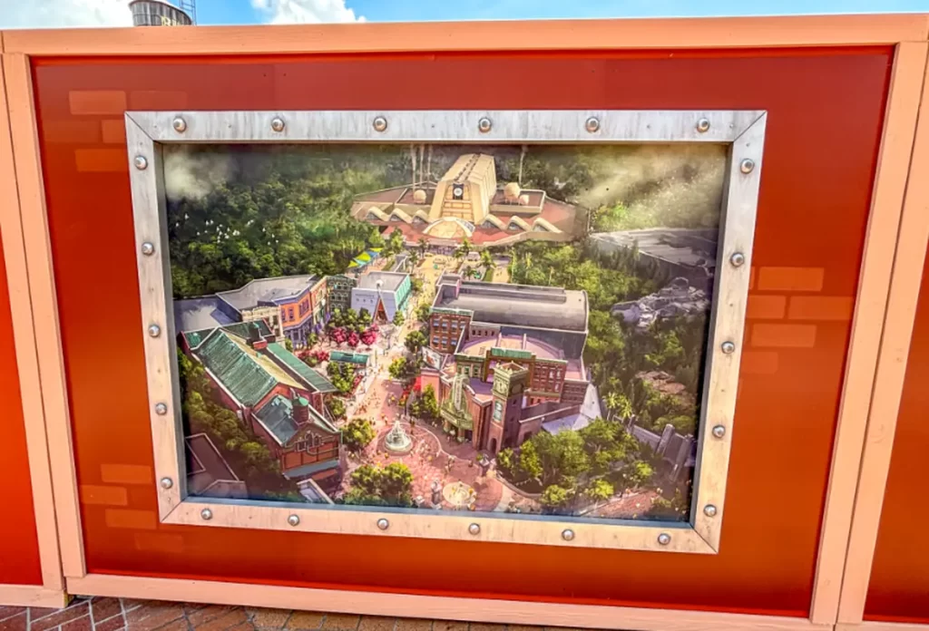 Painel com arte conceitual exibindo a nova área de Monstros S.A. que está sendo construída no Disney’s Hollywood Studios, cercada por vegetação e arquitetura temática.