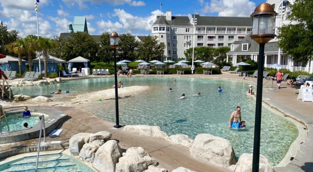 Piscina do Disney’s Yacht Club Resort com área de areia e famílias se divertindo.