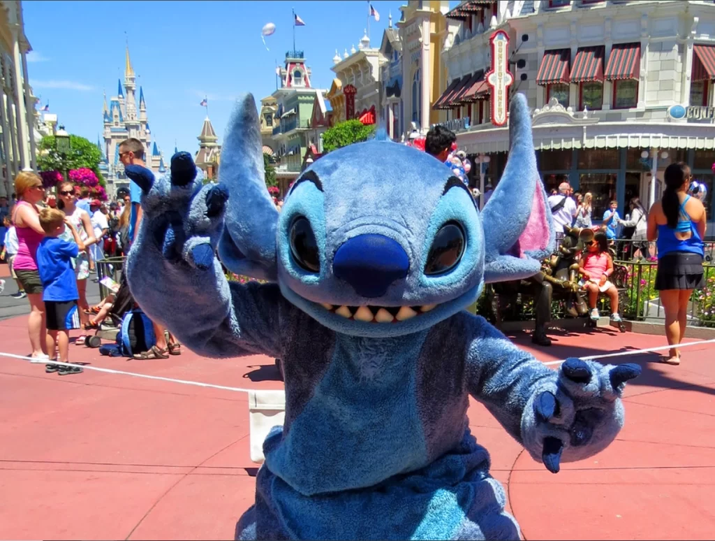 Promoção Ingressos Disney: Stitch no Magic Kingdom, em frente ao castelo da Disney, interagindo com os visitantes.