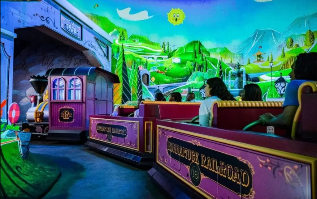 Visitantes no trenzinho da atração Mickey & Minnie's Runaway Railway cercados por cenários animados.