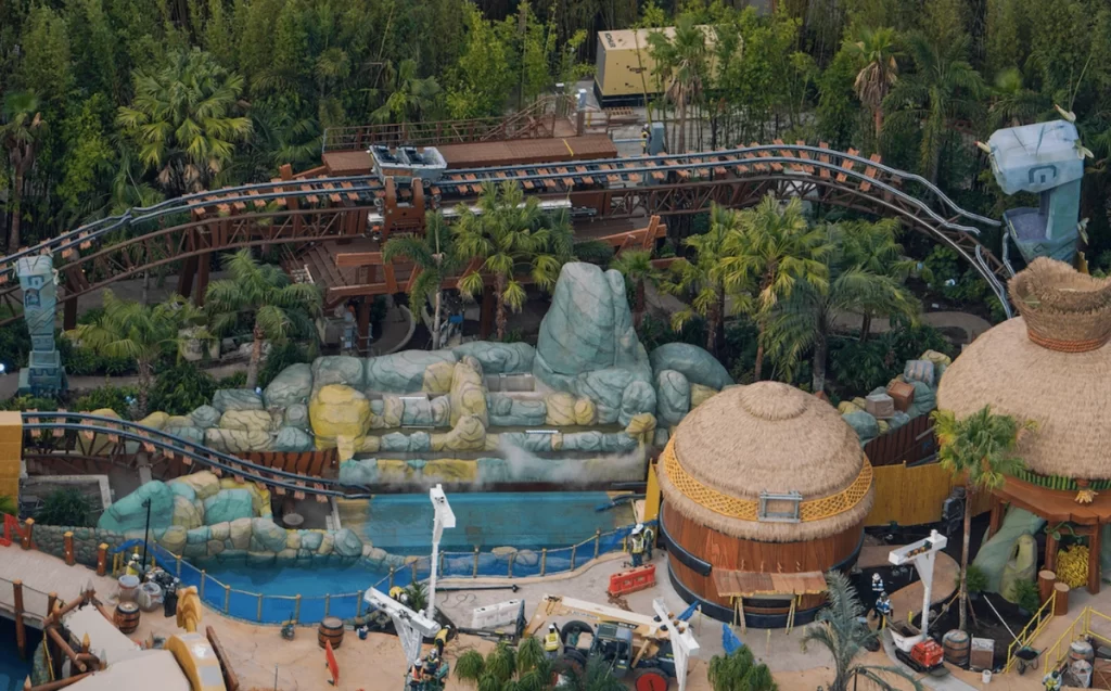 Montanha-russa aquática com temática tiki cercada por vegetação tropical e elementos de construção