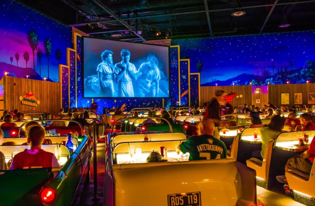 Ambiente do Sci-Fi Dine-In Theater, com mesas em carros antigos assistindo filmes vintage no Hollywood Studios.