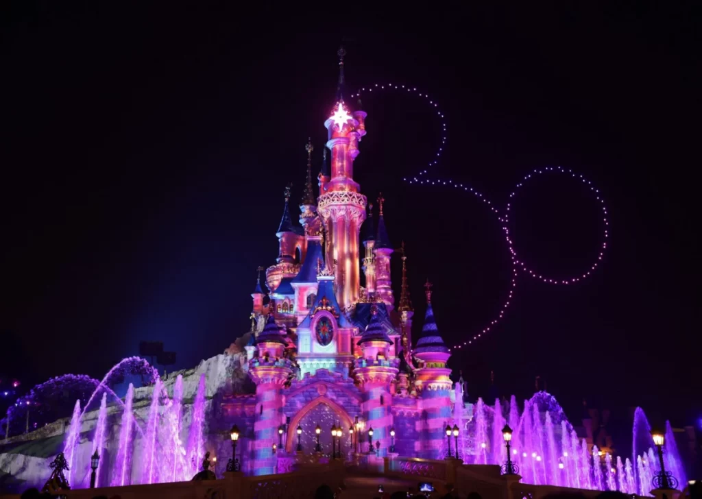 Show noturno da Disneyland Paris com drones formando o rosto do Mickey acima do Castelo da Bela Adormecida iluminado.