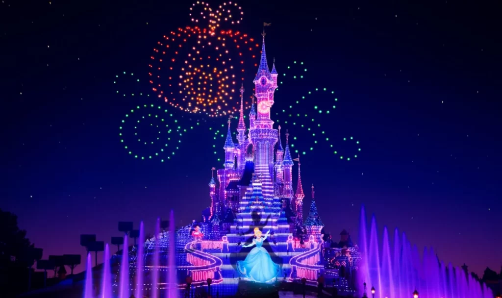 Castelo da Cinderela na Disneyland Paris iluminado com projeções e drones formando uma abóbora mágica no céu.