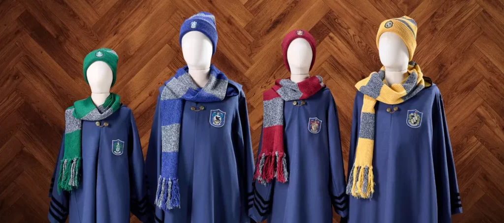 Uniformes das casas de Hogwarts expostos em loja do Epic Universe. Escolha seu lado: Grifinória, Sonserina, Corvinal ou Lufa-Lufa.