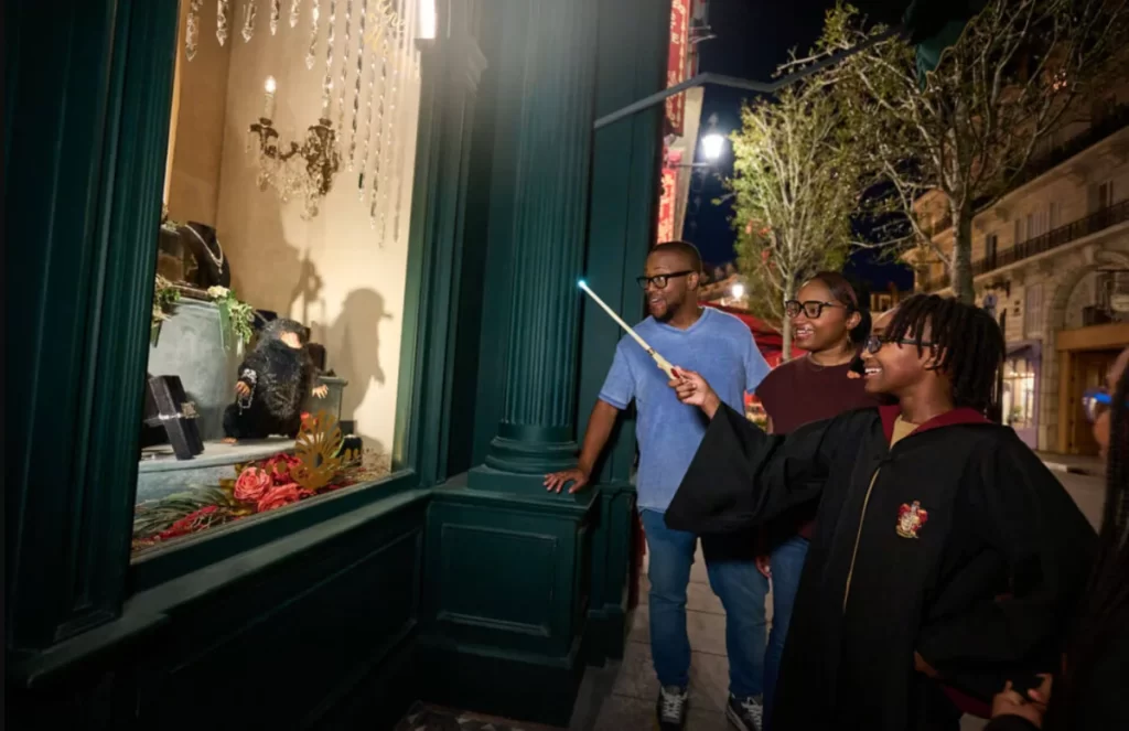 Visitante usando varinha interativa em vitrine com Niffler na área de Harry Potter do Epic Universe