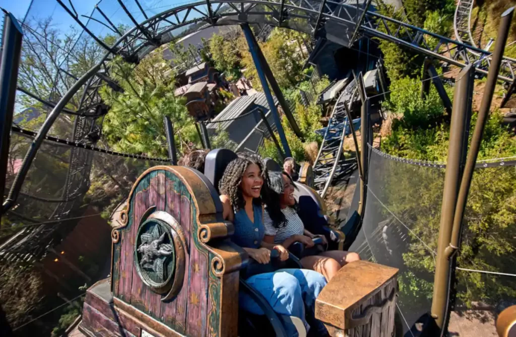 Pessoas sorrindo na montanha-russa Werewolf em meio ao cenário florestal do Epic Universe.