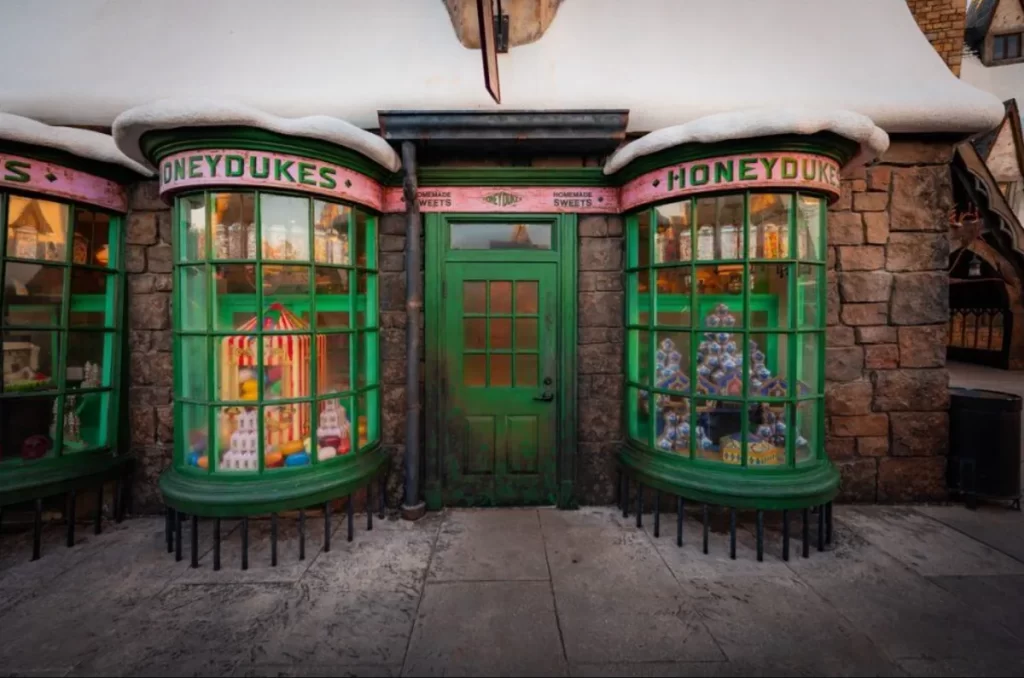 Fachada da Honeydukes em Hogsmeade no Universal Orlando, doceria do Harry Potter com vitrines verdes e telhados nevados