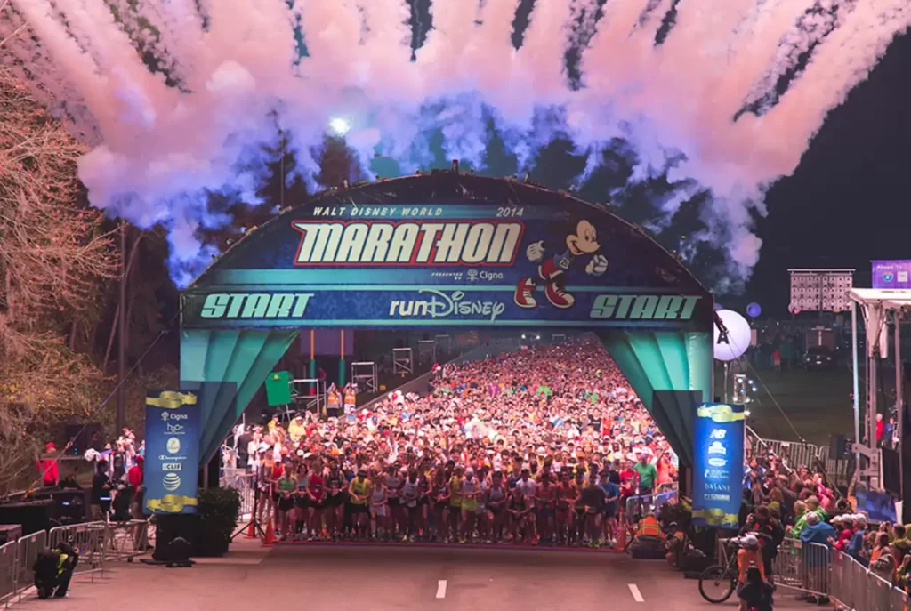 Multidão de corredores na largada da Walt Disney World Marathon com fogos de artifício iluminando o céu.