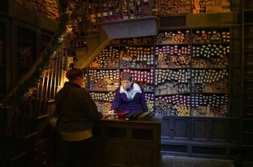 Funcionária de Ollivanders ajudando um visitante a escolher sua varinha