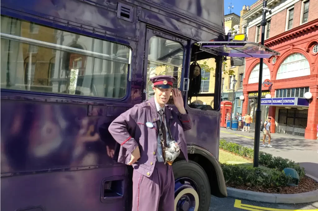 Cobrador do Nôitebus posando ao lado do ônibus roxo de três andares.