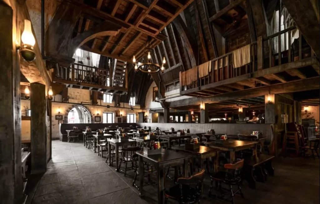 Interior do Três Vassouras com mesas de madeira e teto arqueado em estilo medieval no vilarejo de Hogsmeade.