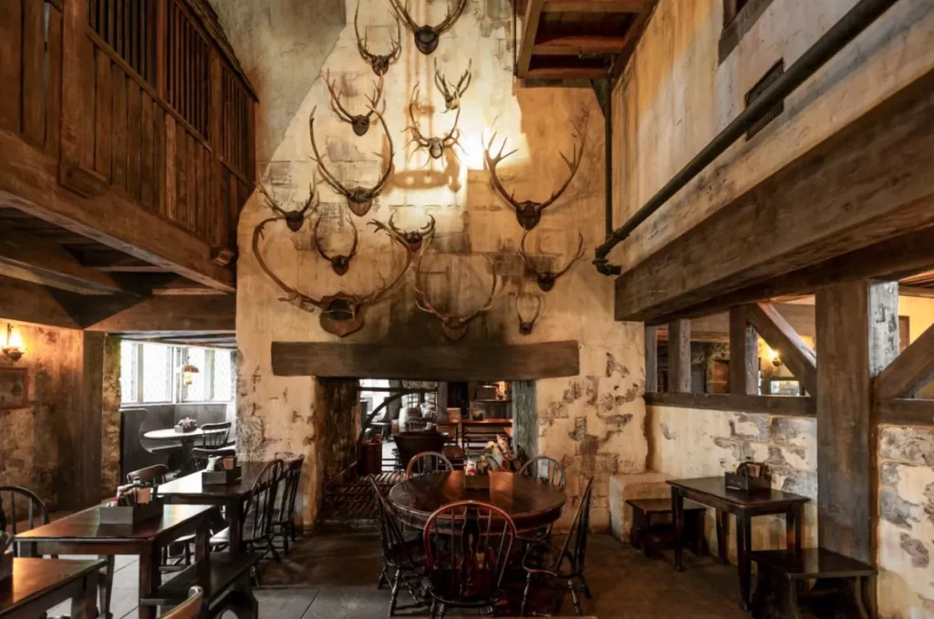 Lareira do Três Vassouras decorada com chifres de cervo e mesas de madeira rústicas.