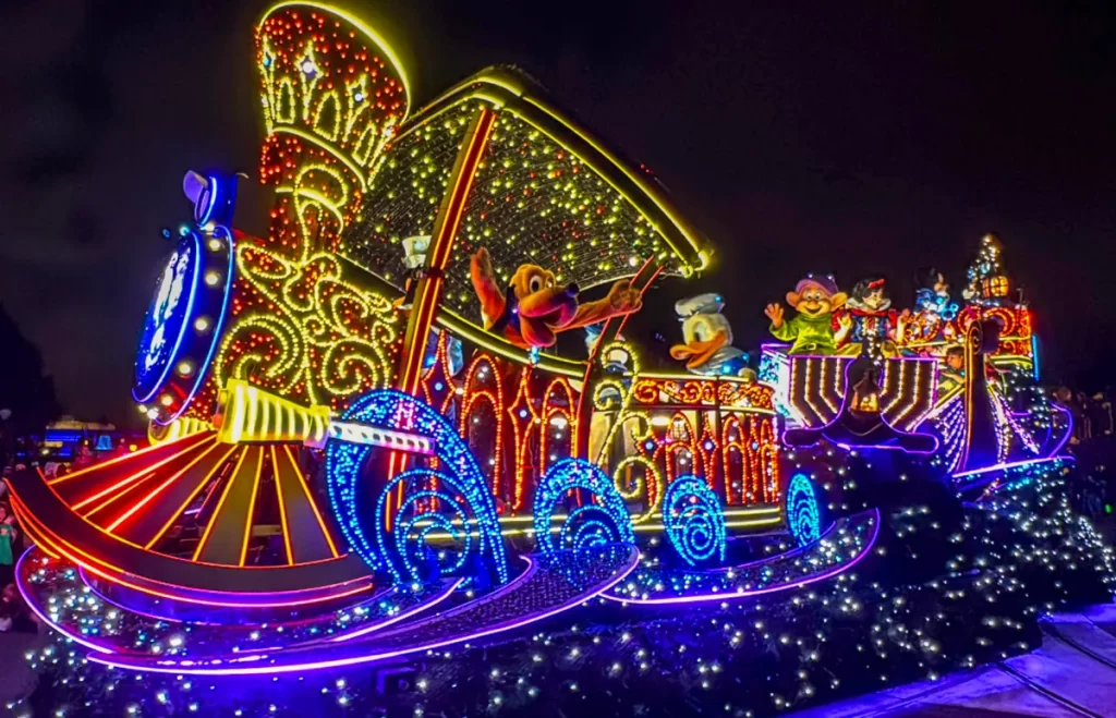Pluto e Pato Donald no carro iluminado do desfile elétrico da Disney, com milhares de luzes coloridas brilhando à noite.