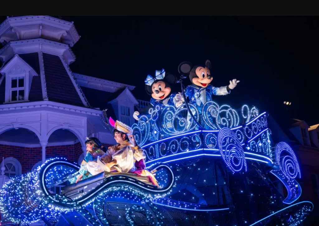 Carro alegórico do desfile Disney Starlight Parade com Mickey e Minnie Mouse ao lado de Aladdin e Jasmine sob luzes azuis brilhantes.