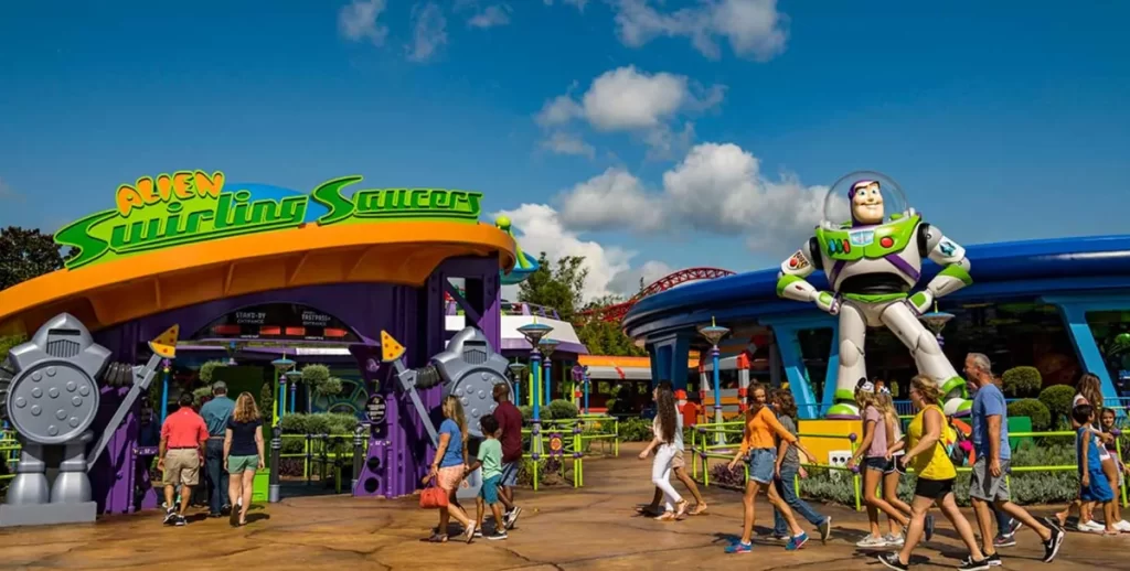 Entrada da atração Alien Swirling Saucers na Disney, com a estátua gigante do Buzz Lightyear e visitantes entrando no parque Toy Story Land.