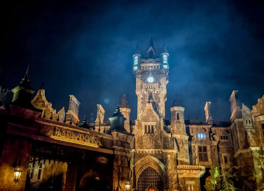 Castelo gótico de Frankenstein no Dark Universe do Epic Universe iluminado à noite, com torre e portão de entrada.