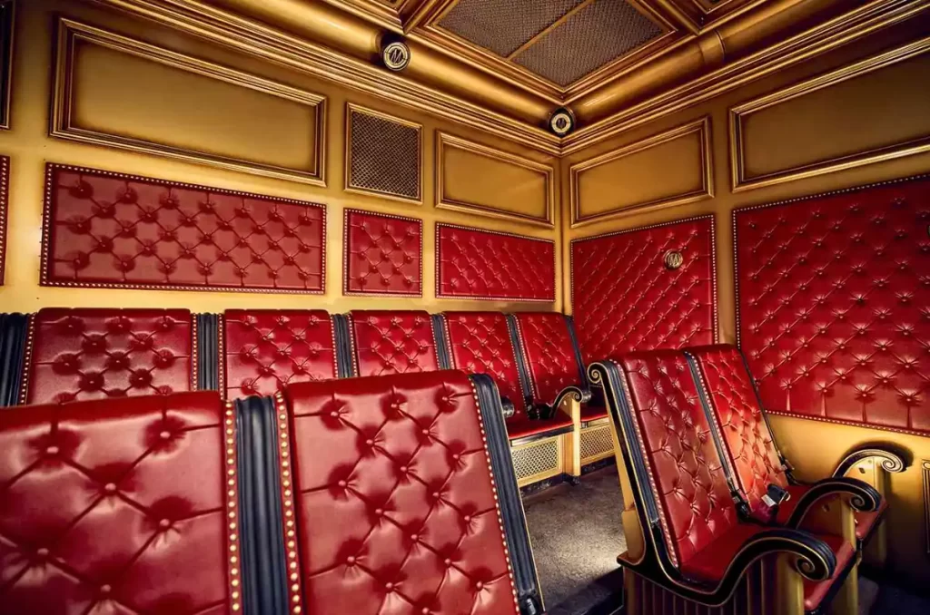 Assentos acolchoados vermelhos e dourados na fila da atração do Ministério da Magia no Epic Universe.