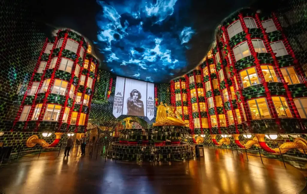 Filmes Para Assistir Antes de Ir a Universal Orlando -Atrium do Ministério da Magia no Epic Universe, mosaicos verdes, janelas iluminadas, fonte dourada e teto com nuvens mágicas.