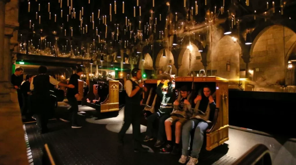 Área de embarque da atração “Harry Potter and the Forbidden Journey” — visitantes sentados em bancos encantados sob velas flutuantes.