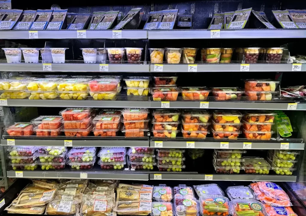 Sessão de frutas frescas na Walgreens com potes de abacaxi, melancia e mix de frutas cortadas.