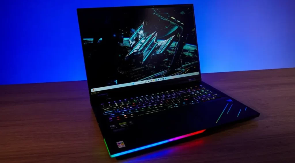 Notebook gamer aberto sobre uma mesa, com teclado RGB colorido, tela grande exibindo gráficos futuristas e iluminação LED na parte frontal.