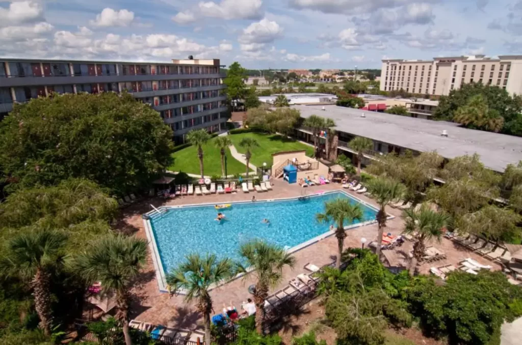 Vista aérea da piscina do Rosen Inn International Drive com hóspedes e jardins ao redor.