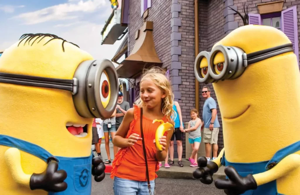 Criança interagindo com dois Minions em área temática da Universal Studios.
