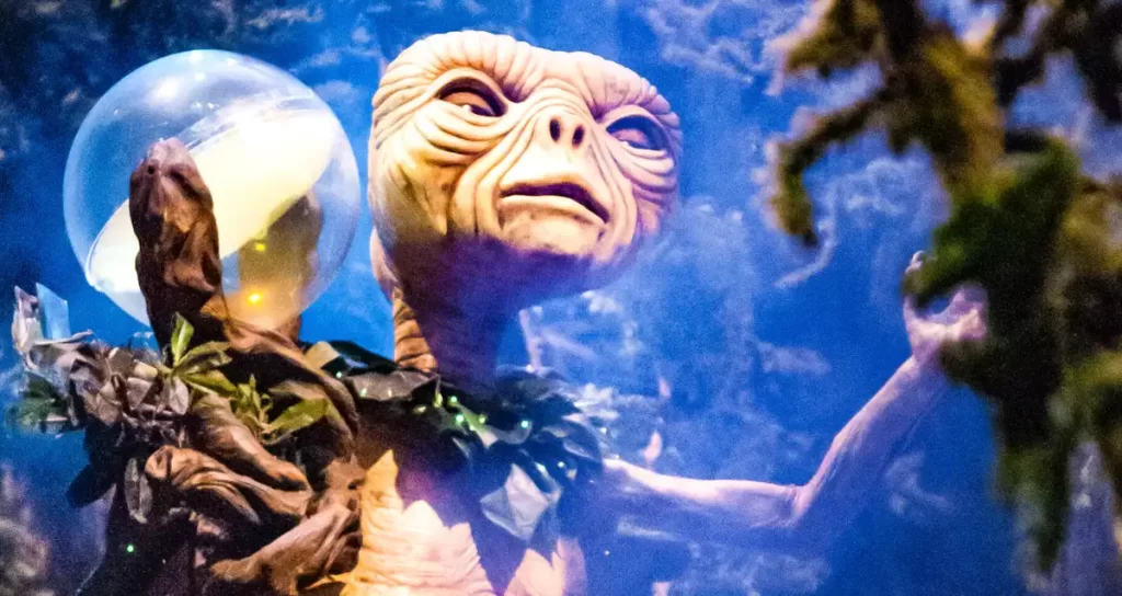 Cena interna da atração ET Adventure com visitantes pedalando bicicletas suspensas.