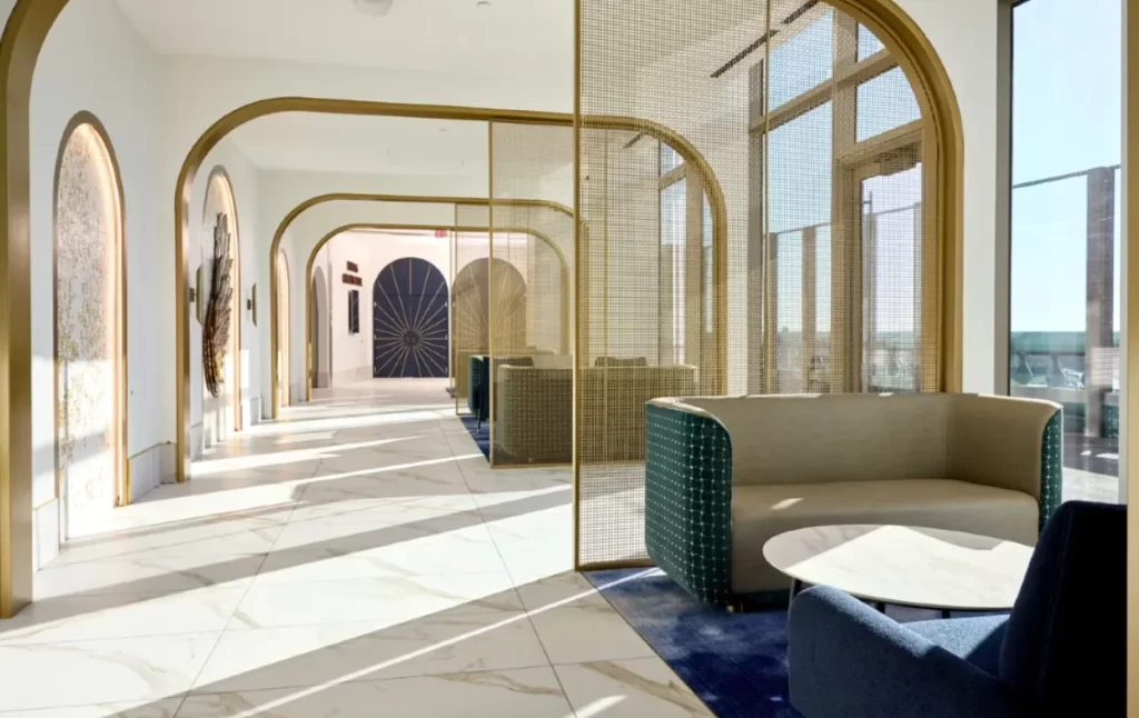 Área lounge do Helios Grand Hotel Epic Universe Orlando com arcos dourados, luz natural e ambiente moderno e luxuoso