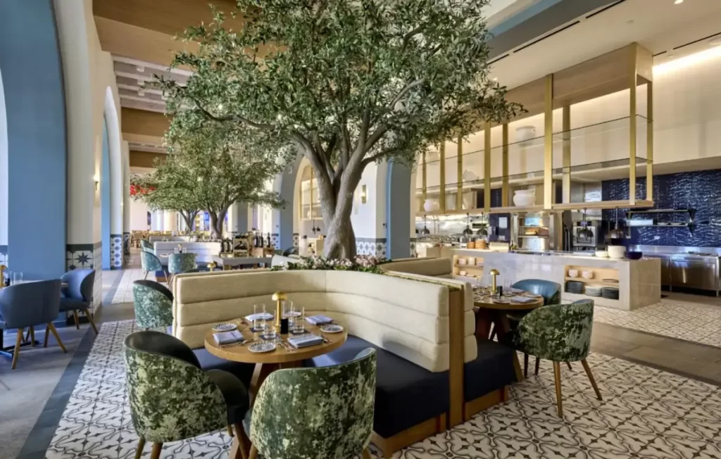 Restaurante sofisticado do Helios Grand Hotel Epic Universe Orlando, com design elegante, árvores internas e cozinha aberta