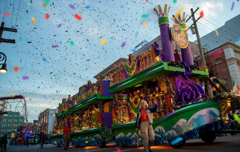 Desfile Mardi Gras Universal Orlando com carro alegórico roxo, verde e dourado e chuva de confete