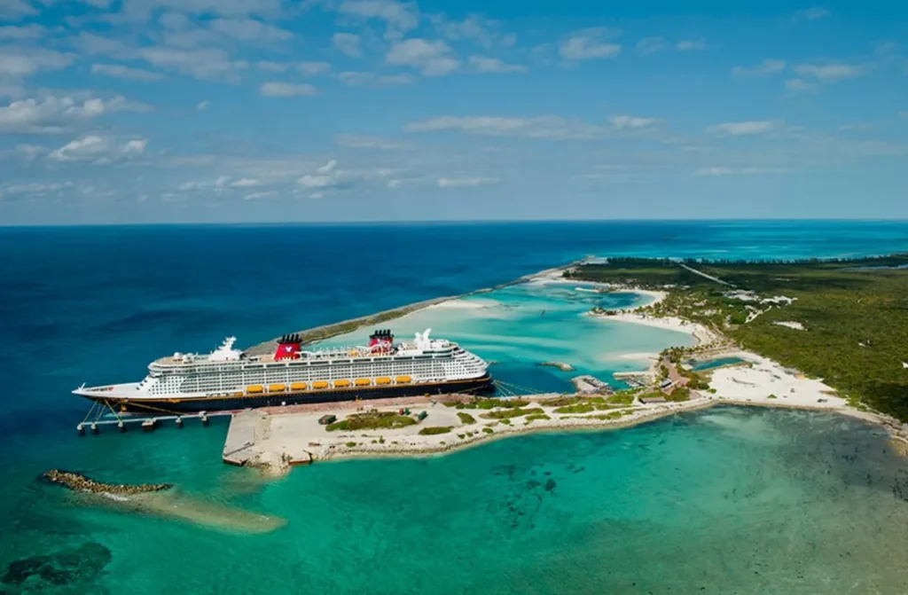 Navio Disney Cruise Line atracado no pier de Castaway Cay, ilha privativa nas Bahamas, com o oceano Atlântico de um lado e a lagoa turquesa da ilha do outro, visto de drone