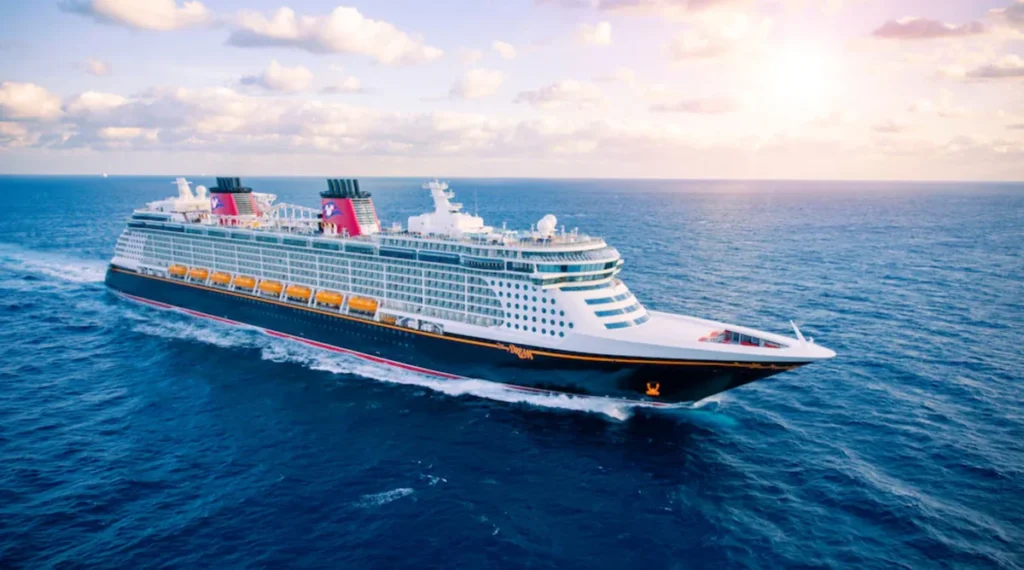 Cruzeiro Disney navegando em alto-mar durante o pôr do sol, com o navio da Disney Cruise Line visto de lado em águas azuis.