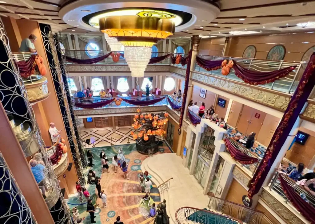 Átrio do cruzeiro Disney Magic com decoração elegante, lustre central e vários andares com hóspedes