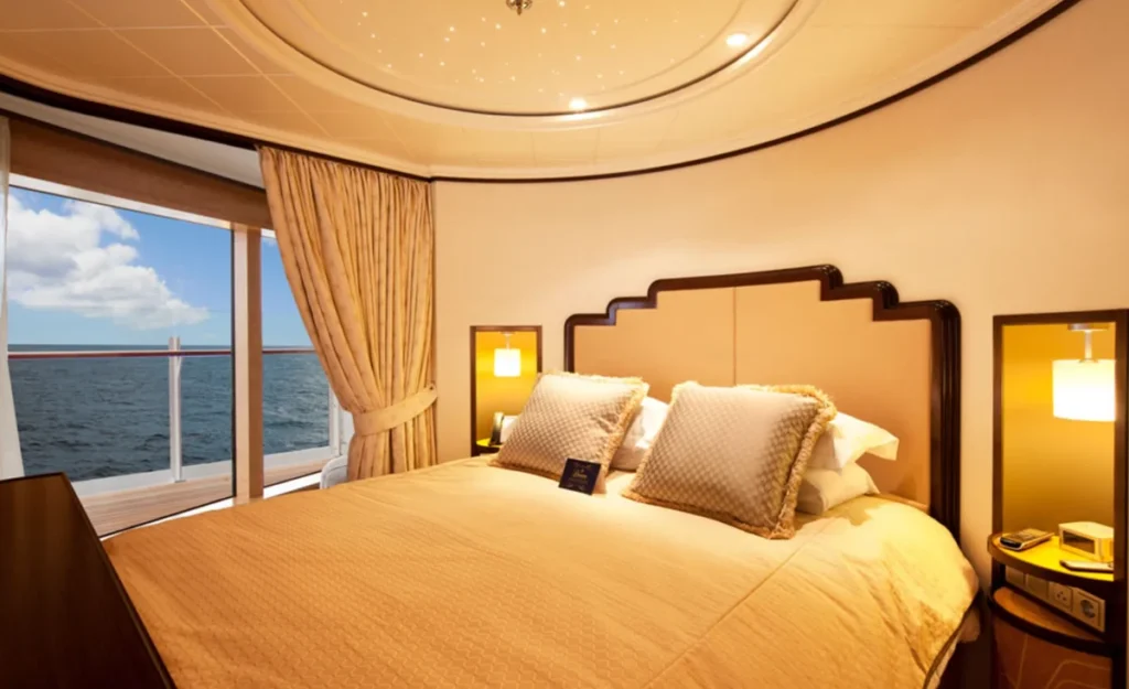 Cabine luxuosa do Disney Magic com iluminação suave e varanda com vista para o mar.