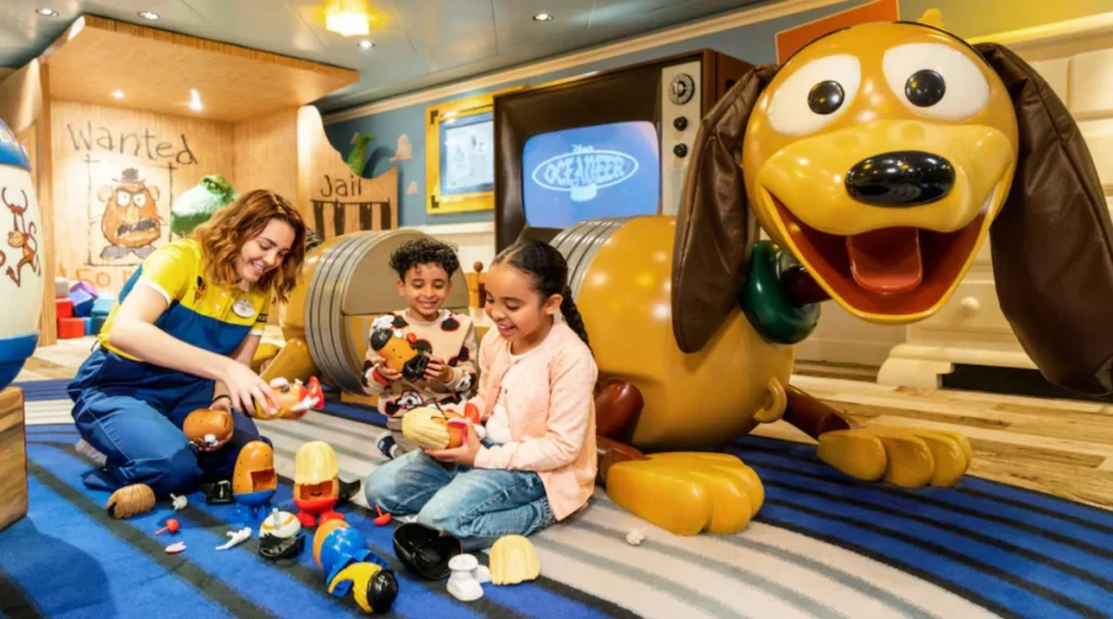 Área infantil temática Toy Story com crianças brincando e escultura do Pluto em cruzeiro Disney.
