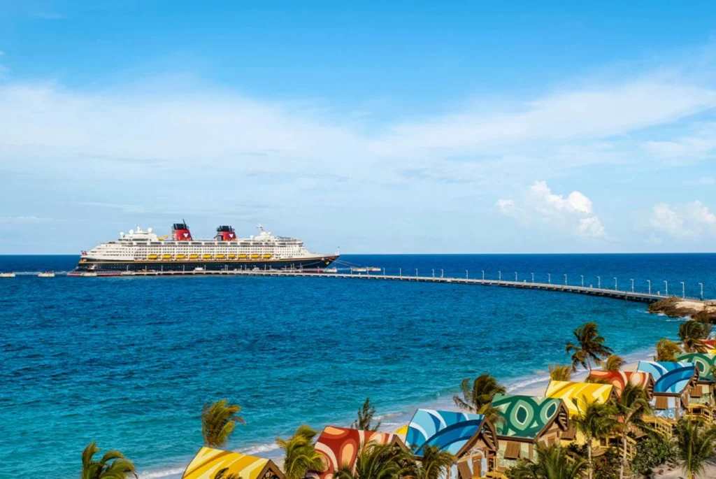 Vista panorâmica de Disney Lookout Cay at Lighthouse Point, com o navio da Disney atracado diante do mar cristalino das Bahamas.