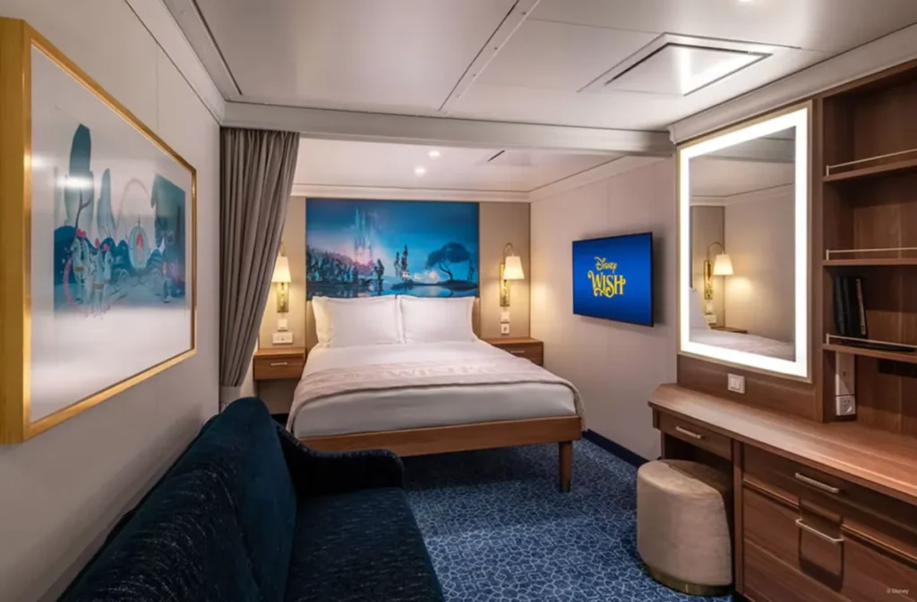 Cabine interna elegante do navio Disney Wish com cama de casal, sofá e decoração temática Disney.