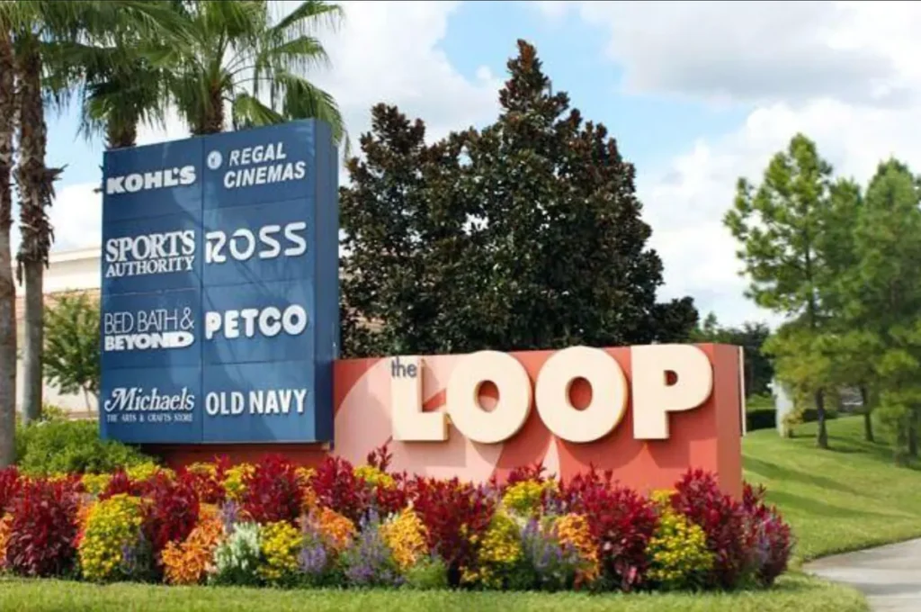 Entrada principal do The Loop Orlando em Kissimmee, na Flórida, com placas de lojas como Ross, Kohl's, Old Navy e Regal Cinemas.
