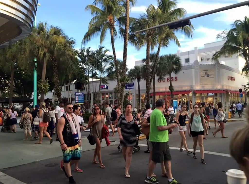 Pedestres atravessam uma área comercial movimentada da Lincoln Road, cercada por lojas e palmeiras.