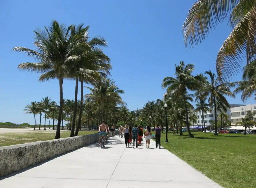 Visitantes caminham pelo passeio arborizado do Lummus Park, entre a praia e os edifícios de Ocean Drive.