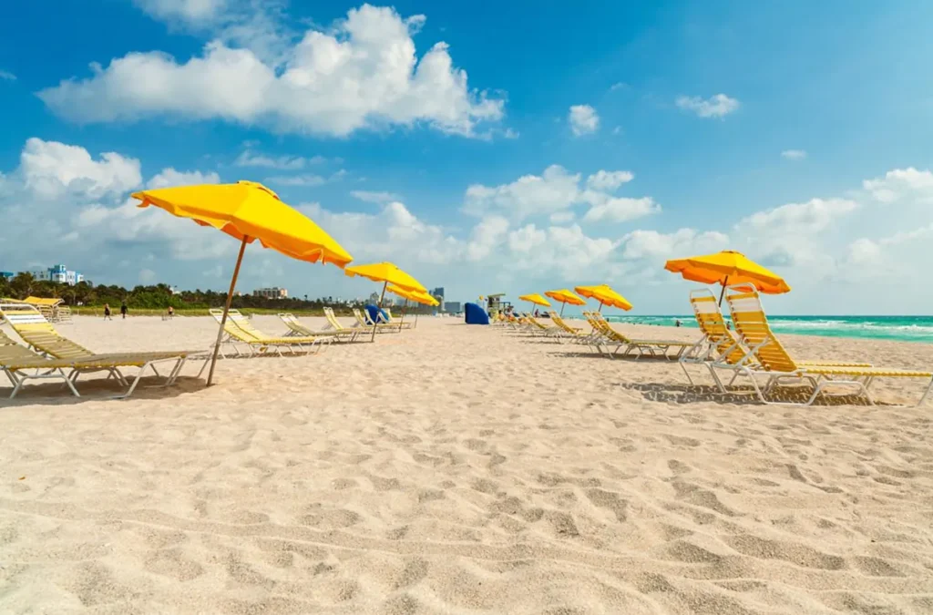 Cadeiras e guarda-sóis amarelos organizados na areia de South Beach, com o Oceano Atlântico ao fundo.