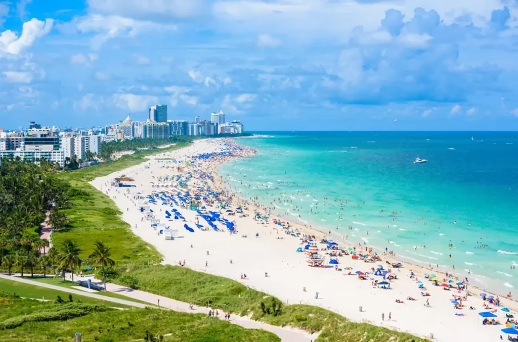 Panorama de South Beach com águas claras, praia movimentada e edifícios de Miami Beach ao longo do litoral.