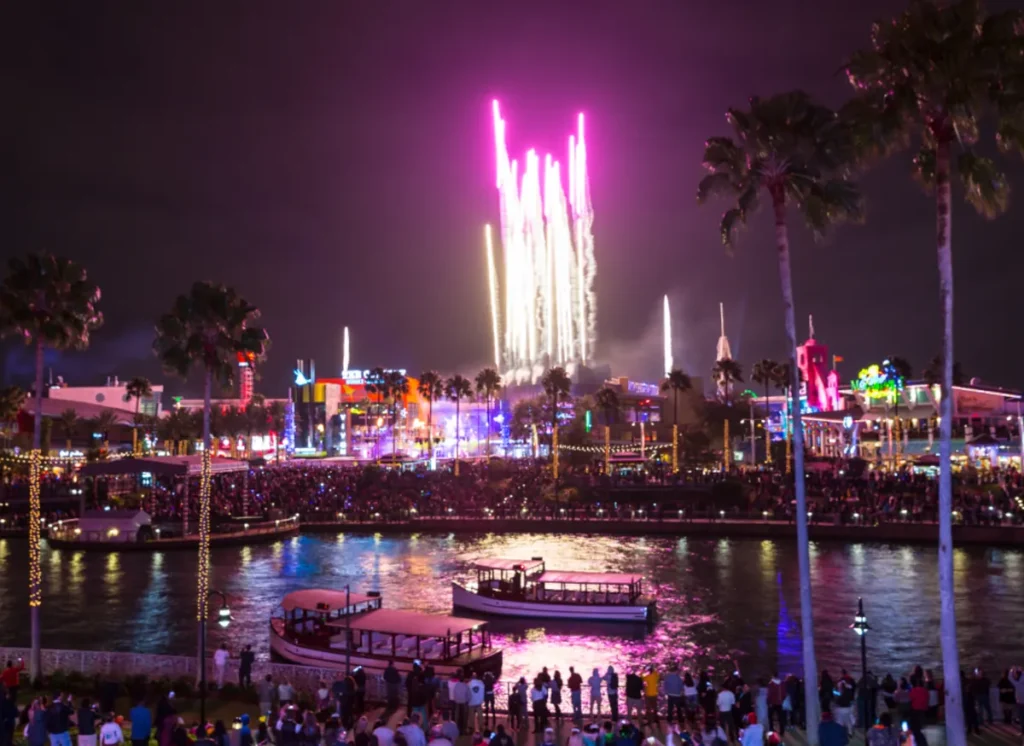 Fogos de Ano Novo Universal Orlando 2026 com público reunido no CityWalk e reflexos coloridos sobre o lago.