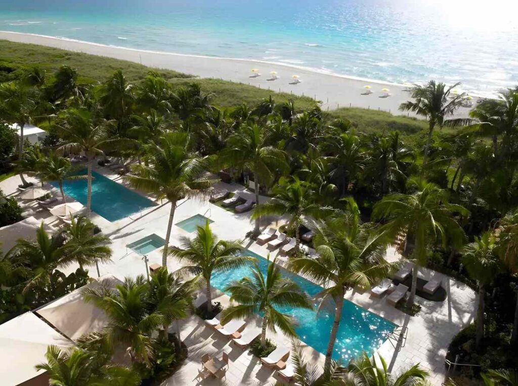 Área de piscinas do Grand Beach Hotel Miami Beach cercada por palmeiras e localizada próxima à praia.