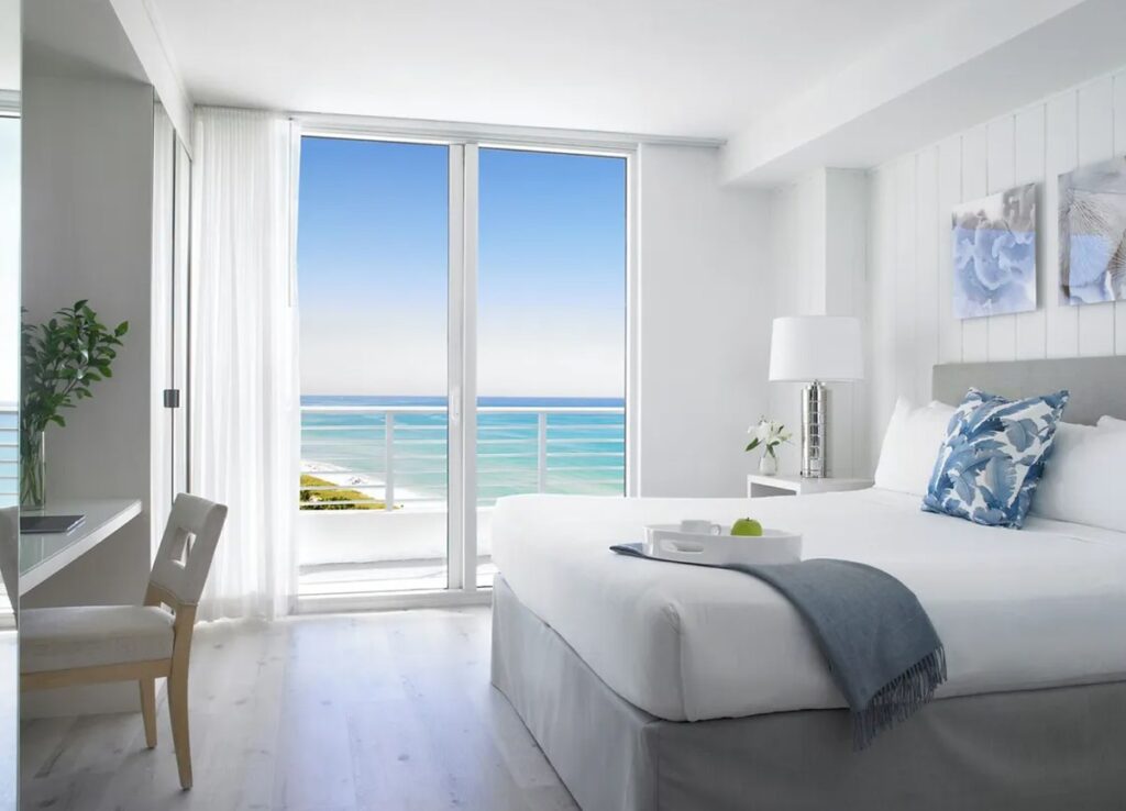 Quarto claro e moderno do Grand Beach Hotel Miami Beach com varanda e vista para o mar.