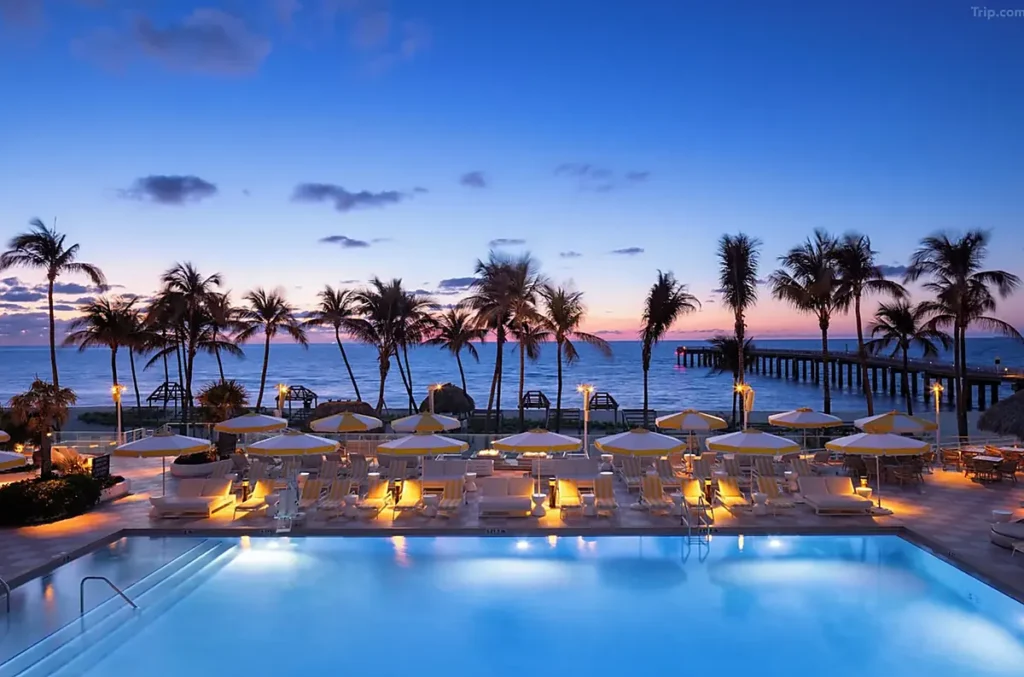 Piscina do The Sunny Miami à beira-mar em Sunny Isles Beach, com espreguiçadeiras, palmeiras e vista para o oceano ao entardecer.