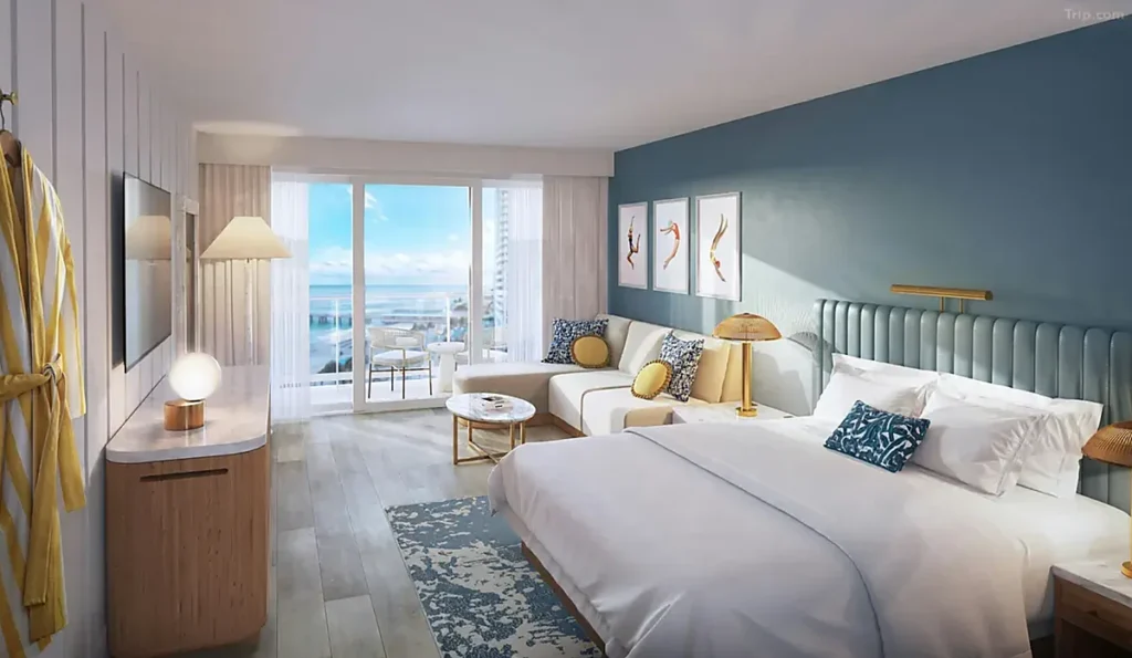 Quarto do The Sunny Miami em Sunny Isles Beach, com cama de casal, sofá, decoração em tons de azul e varanda com vista para o oceano.